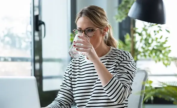 Mulher bebe um copo de água enquanto trabalho num computador portátil